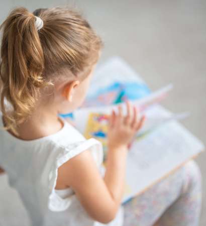 Cute little girl is sitting and leafing through a book with fairy tales. High quality photo